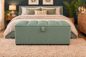 A mint green upholstered storage bench with tufted back cushions sits at the foot of a bed in a styled bedroom setting with a shag rug, wooden nightstands, and plants.